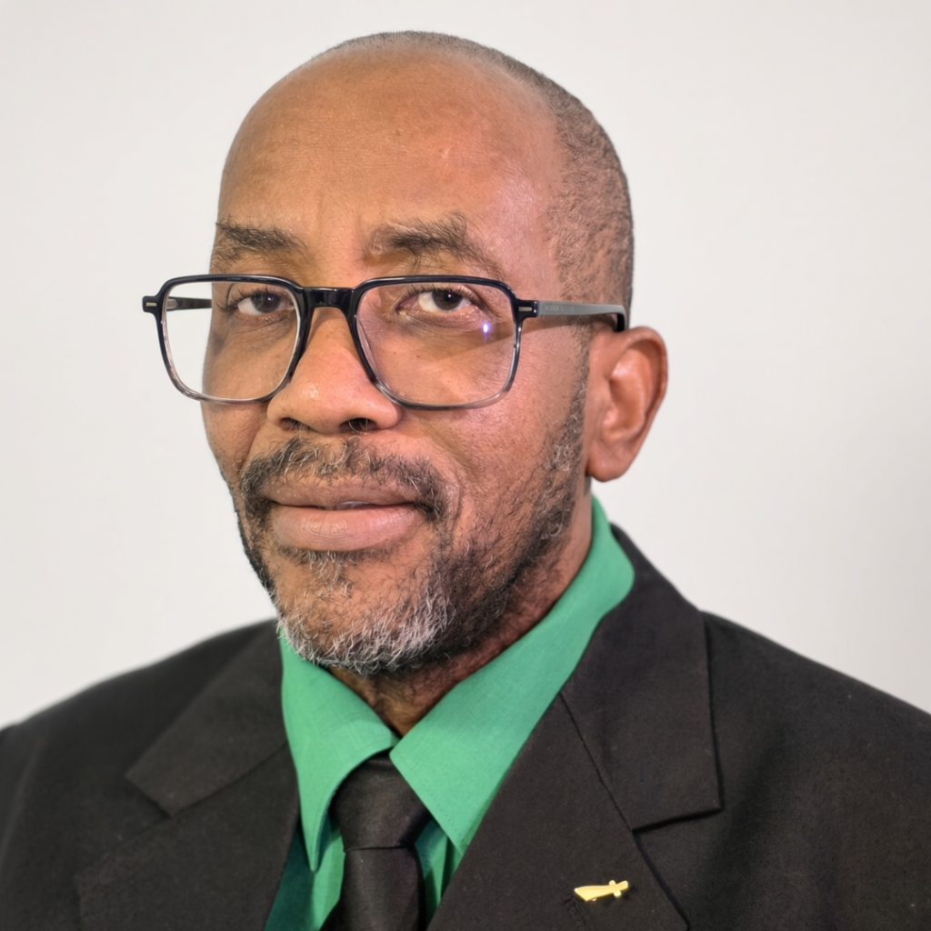 Close-up portrait of a Black man wearing glasses, a black suit, green shirt, and black tie.