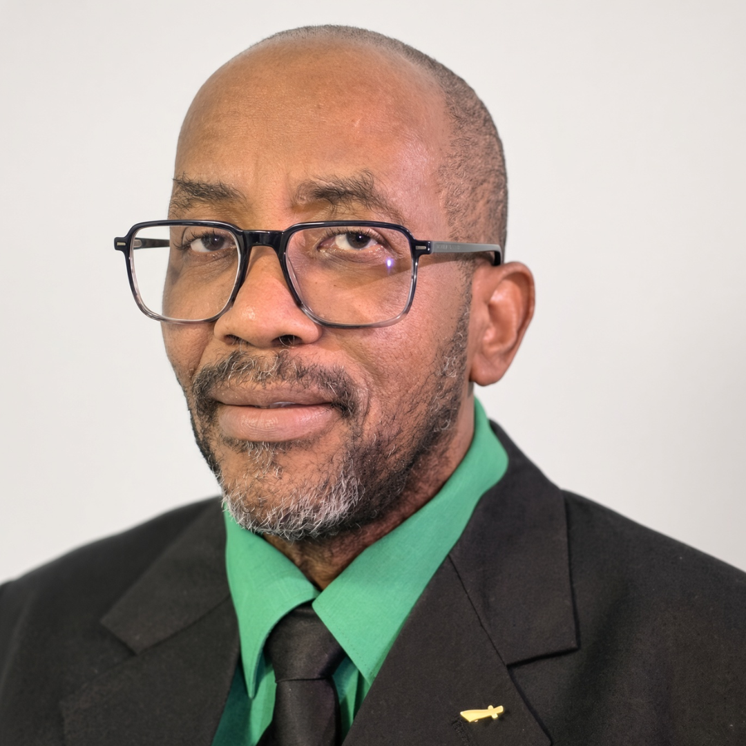 Close-up portrait of a Black man wearing glasses, a black suit, green shirt, and black tie.