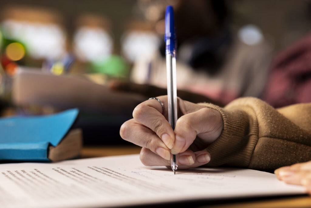 Close-up of a hand holding a blue pen, ready to write on a printed document at a desk.